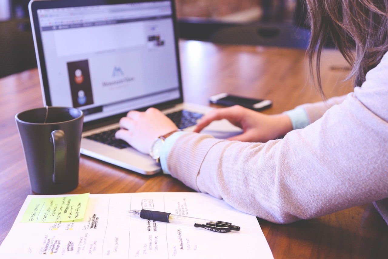 Lady working on a laptop with a notepad and pen alongside her arm